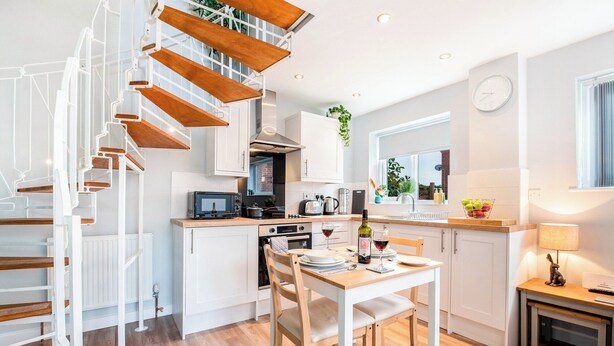 A modern kitchen with a wooden staircase, white cabinetry, and a dining area with a table set for two. - 1 bedroom accommodation in Acomb, near York (Acomb, near York)
