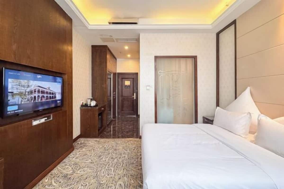 Habitación de hotel con cama, televisor montado en la pared, escritorio y puerta de baño.