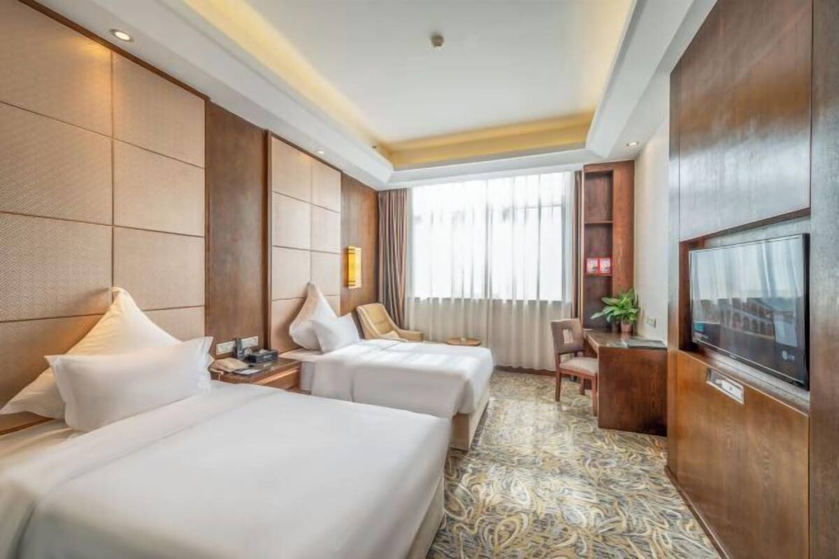 Habitación de hotel con dos camas, televisión, escritorio y ventana con cortinas.