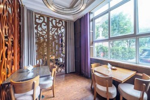 Un comedor con mesas y sillas de madera, un biombo decorativo y vistas a través de amplios ventanales.