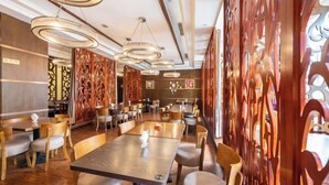 A restaurant with wooden tables and chairs, decorative wall panels, and modern pendant lighting. - Jia Lian Hotel (Daozhen)