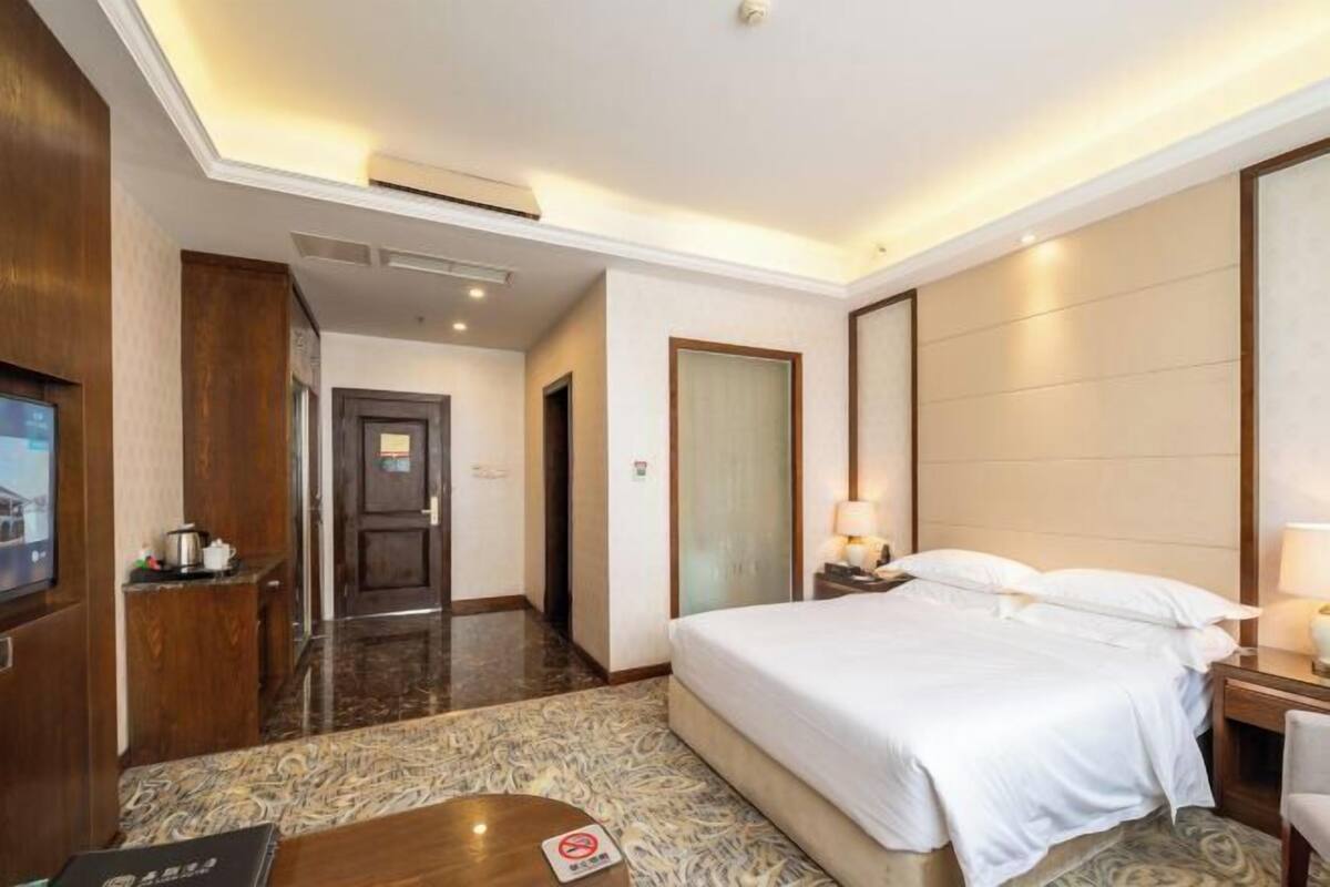 Una habitación de hotel con una cama, mesita de noche, lámpara y televisión en la pared.