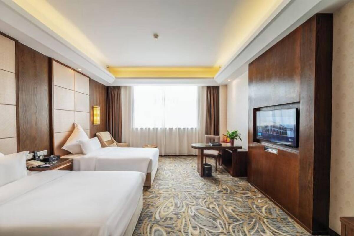 Habitación de hotel con dos camas, un televisor, un escritorio con silla y una alfombra estampada.