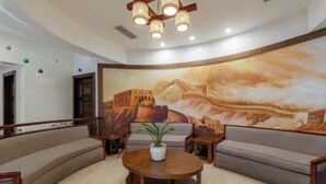A lobby with a large mural, a round wooden table, and two sofas. - Jia Lian Hotel (Daozhen)