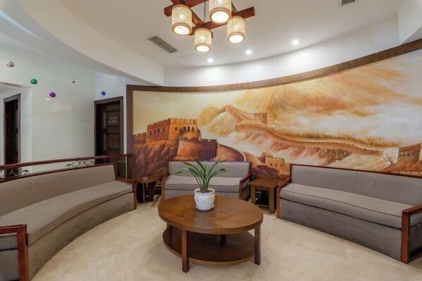 A lobby with a large mural, a round wooden table, and two sofas. - Jia Lian Hotel (Daozhen)
