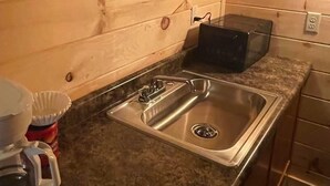 Una cocina con pileta de acero inoxidable, paredes de madera, encimera de granito y microondas.