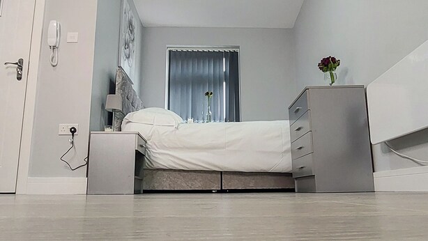 A modern bedroom with a bed, bedside table, lamp, and a dresser. - Charming Accommodation Close to Birmingham (West Bromwich)