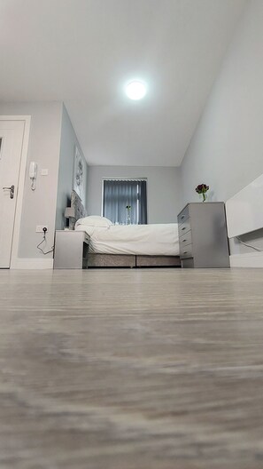 A modern bedroom with a bed, bedside table, lamp, and a dresser.