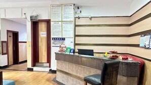 A reception area with a counter, two bar stools, and a wall-mounted information board. - Duyun Jiayuan Hotel (Duyun)