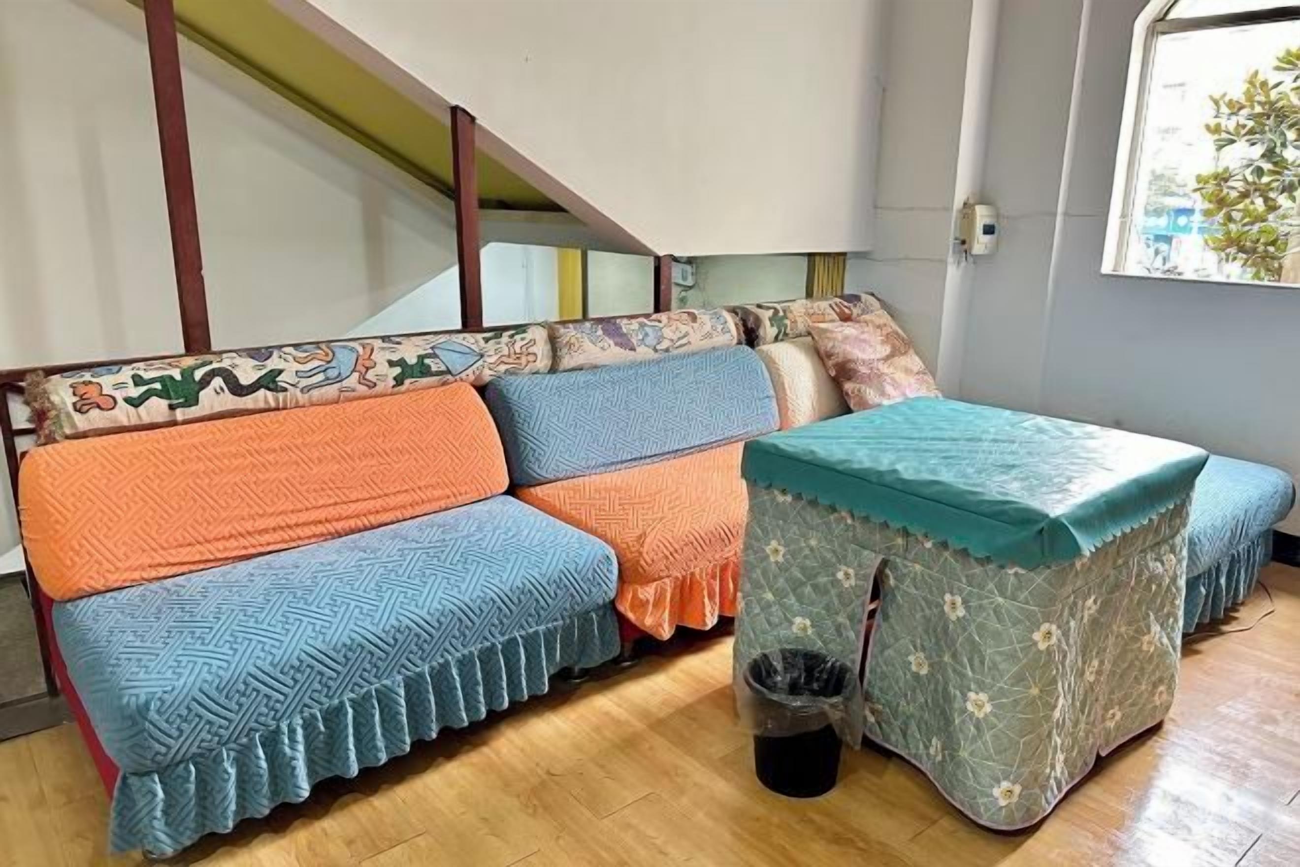 A room with a sofa, ottoman, and a trash bin.