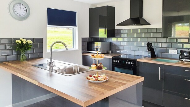 A modern kitchen with a wooden countertop, black cabinets, a stainless steel sink, a built-in oven, and a window with a view of the outdoors. - Kingfisher Lodge - UK40017 (Halwill Junction, near Beaworthy)