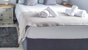 A neatly made bed with a quilted cover, two pillows, and rolled towels on a dark-colored bedspread. - Kingfisher Lodge - UK40017 (Halwill Junction, near Beaworthy)