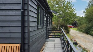 A wooden building with a balcony, a bench, and a gravel path leading to a red car. - Kingfisher Lodge - UK40017 (Halwill Junction, near Beaworthy)