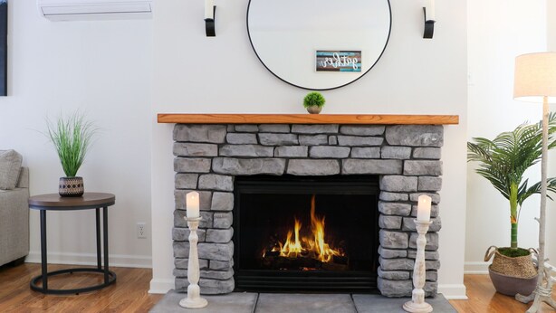 A fireplace with a stone surround, a round mirror above it, and two candles on either side.