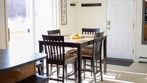 A dining area with a table and chairs, a fruit bowl, and a 'HOME' sign on the wall.