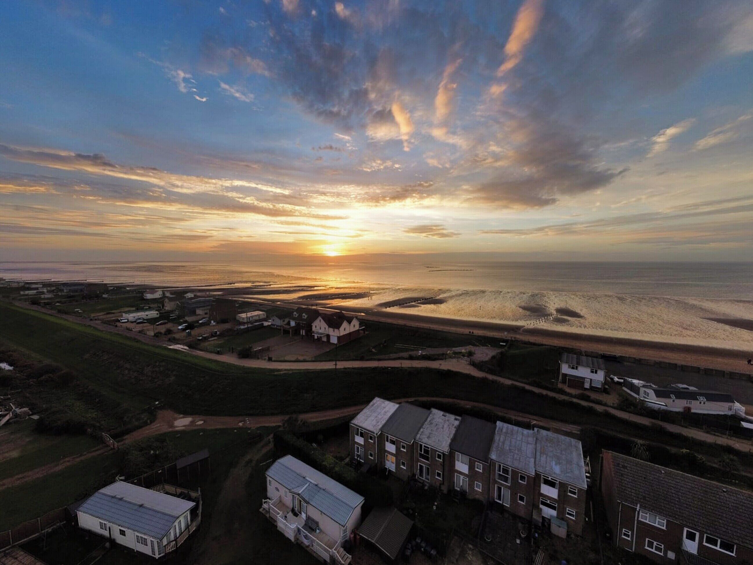 Vue aérienne d’une zone côtière avec des immeubles résidentiels, une plage et un coucher de soleil.