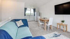 A compact living space with a sofa, dining table, chairs, a TV, and a view through a window. - 2 bedroom accommodation in Hunstanton (Hunstanton)