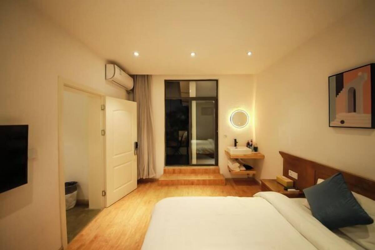 A hotel room with a bed, bedside table, nightstand, and a bathroom with a sink and mirror.