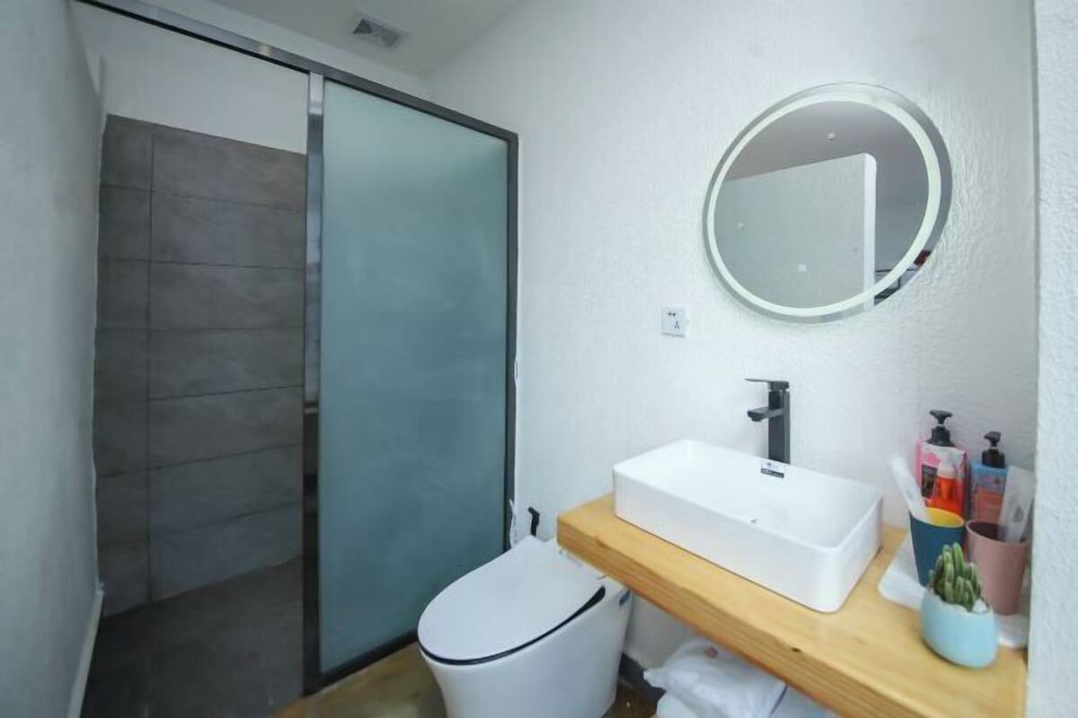 A bathroom with a shower, a white sink, a mirror, and toiletries on a shelf.