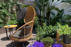 A wicker chair with a cushion, a small round table, and potted plants in a garden setting. - Erduobian Inn (Dali City)