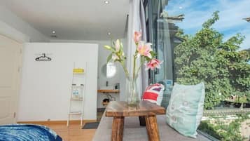 Una habitación moderna con una mesa de madera, un florero con flores, una ventana con vistas a la vegetación y una cama con cubrecama azul.