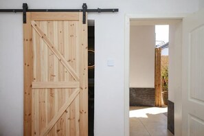 A wooden sliding barn door in a hallway with a view of a bamboo fence and a stone wall outside. - Erduobian Inn (Dali City)