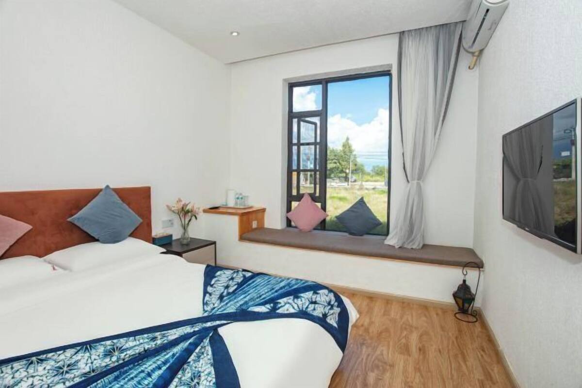 A bedroom with a bed, a window seat, a nightstand, and a wall-mounted TV.