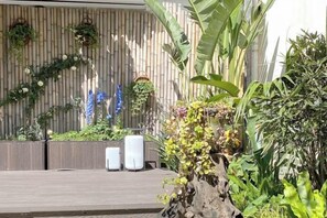 En træterrasse med en bambusvæg, krukker med planter og et vandelement.
