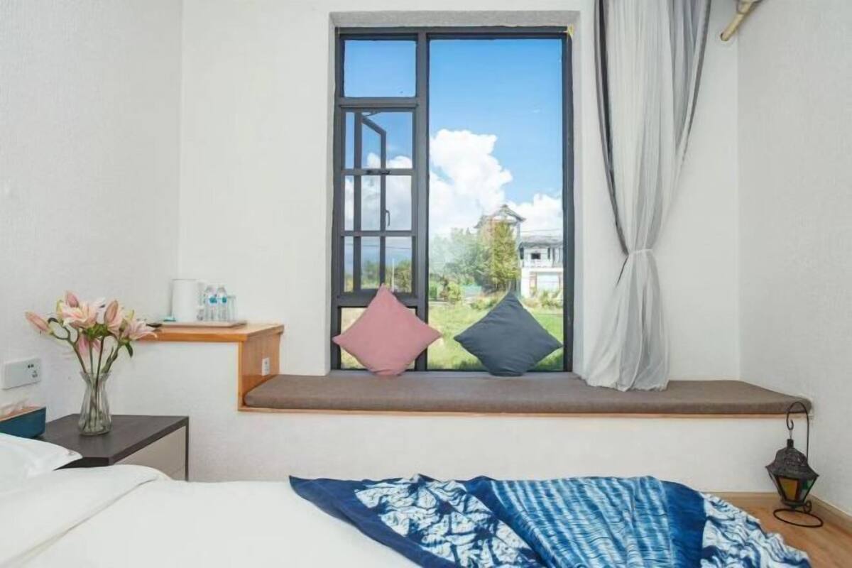 A bedroom with a window seat, a bed, a bedside table with a vase of flowers, and a nightstand with a lantern.