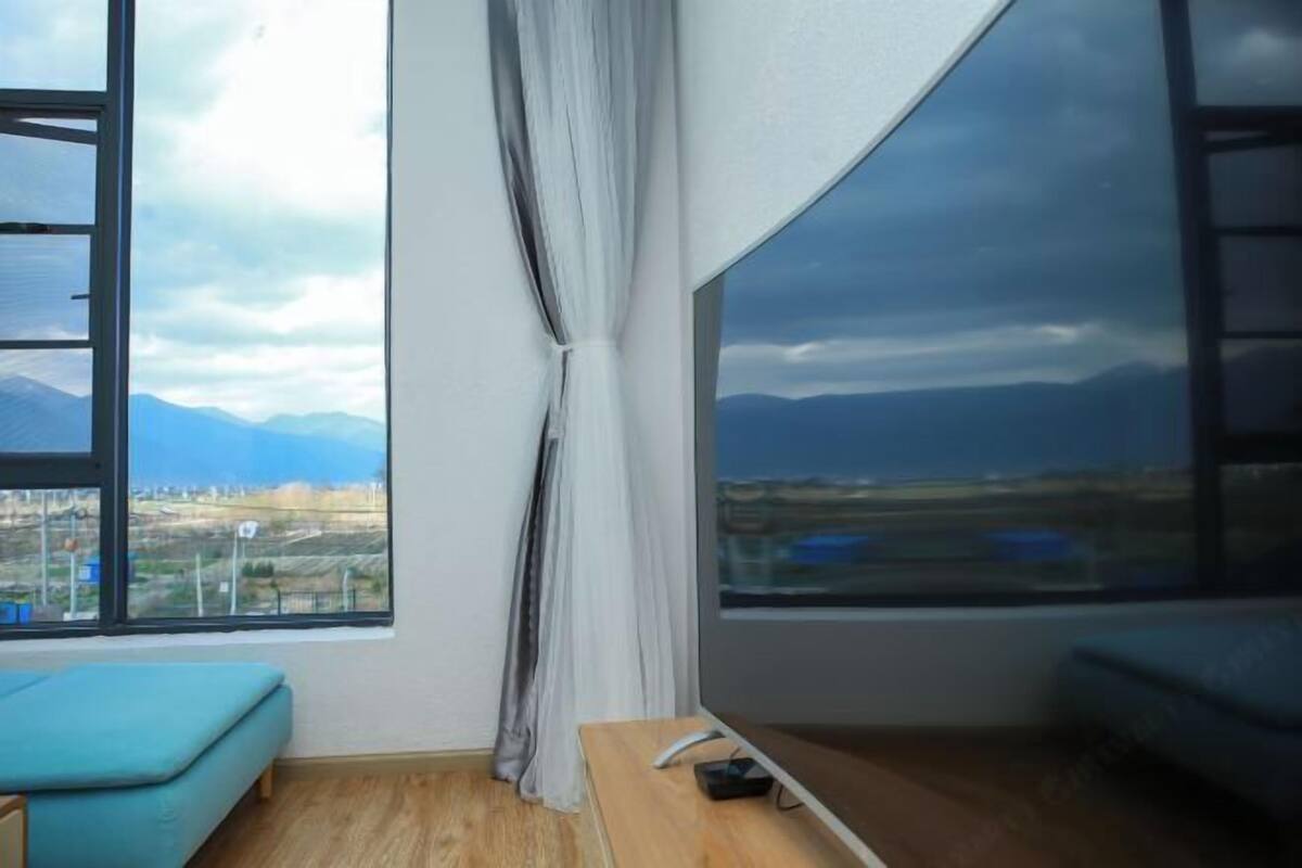 A room with a large window, a wooden bench, a blue sofa, and a curtain.