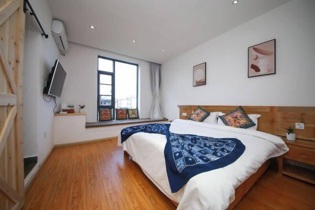 A bedroom with a bed, a window, a TV, and a wall-mounted air conditioner.