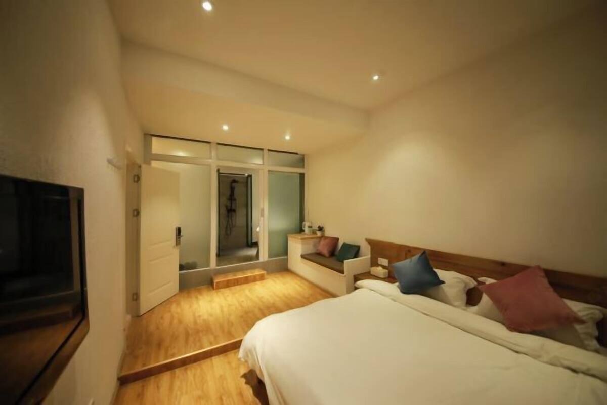 A bedroom with a bed, a TV, a sliding door leading to a bathroom, and a small seating area with cushions.
