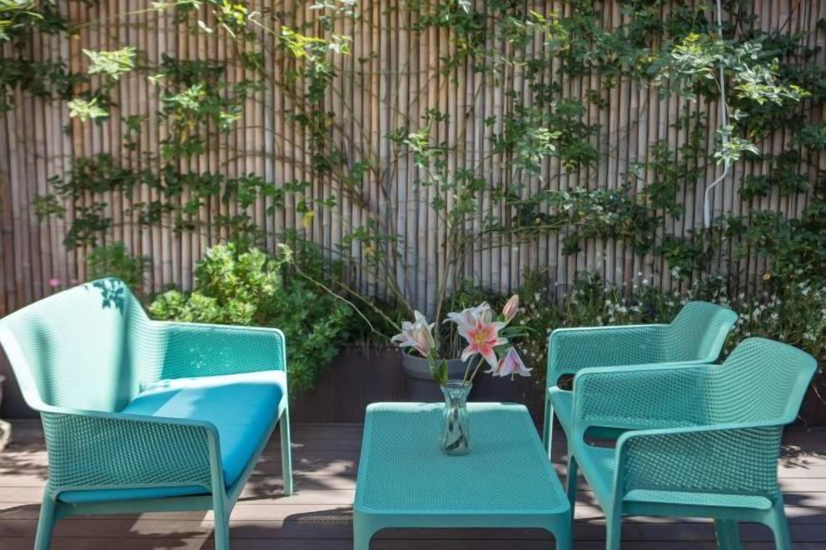A patio with two green chairs and a small table, a bamboo fence, and climbing plants.