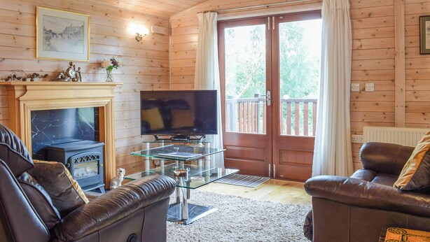 A cozy living room with a fireplace, leather sofas, a flat-screen TV, and a glass coffee table. - 2 bedroom accommodation in Bridgnorth (Bridgnorth)