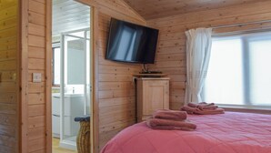 A wooden cabin room with a bed, a television mounted on the wall, and a window with curtains. - 2 bedroom accommodation in Bridgnorth (Bridgnorth)