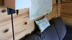 Interior d'una cabana de fusta amb un mapa a la paret, un sofà i dues làmpades penjades.