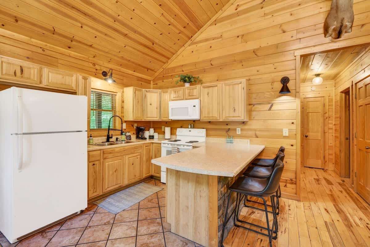A wooden cabin kitchen with a refrigerator, stove, microwave, and bar stools.