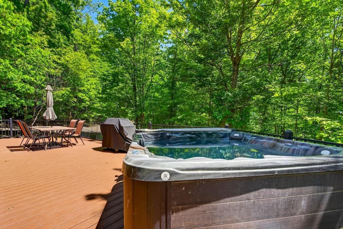 A hot tub on a wooden deck surrounded by lush green trees.