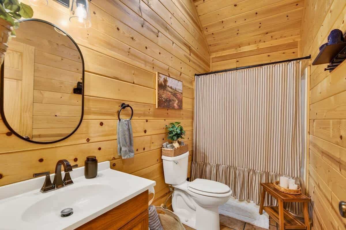 Een houten badkamer met een wastafel, toilet en douchegordijn.