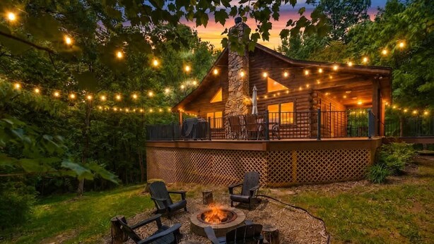 Una cabaña de troncos con una fogata, asientos al aire libre y luces colgantes.