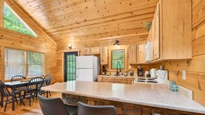 Interior de una cabaña de madera con cocina, comedor y asientos tipo bar.