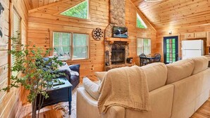 Interior acogedor de una cabaña con chimenea, paredes de madera, un sofá y un comedor.