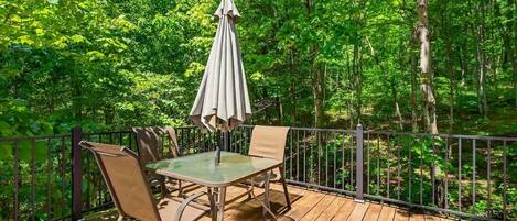 A deck with a table and chairs, surrounded by a metal railing, overlooking a forested area.