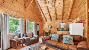 Interior de una cabaña de madera con sala de estar, comedor, cocina y ventanas amplias.