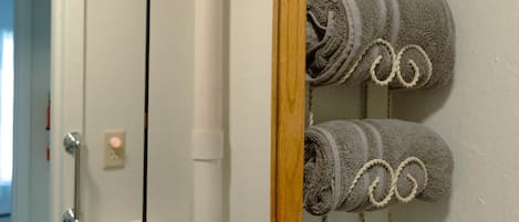 Un baño con un espejo de marco de madera, un perchero con toallas enrolladas y un dispensador de papel higiénico.