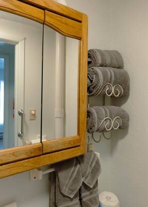 Une salle de bain avec un miroir encadré en bois, un porte-serviettes avec des serviettes pliées et un support à papier toilette.