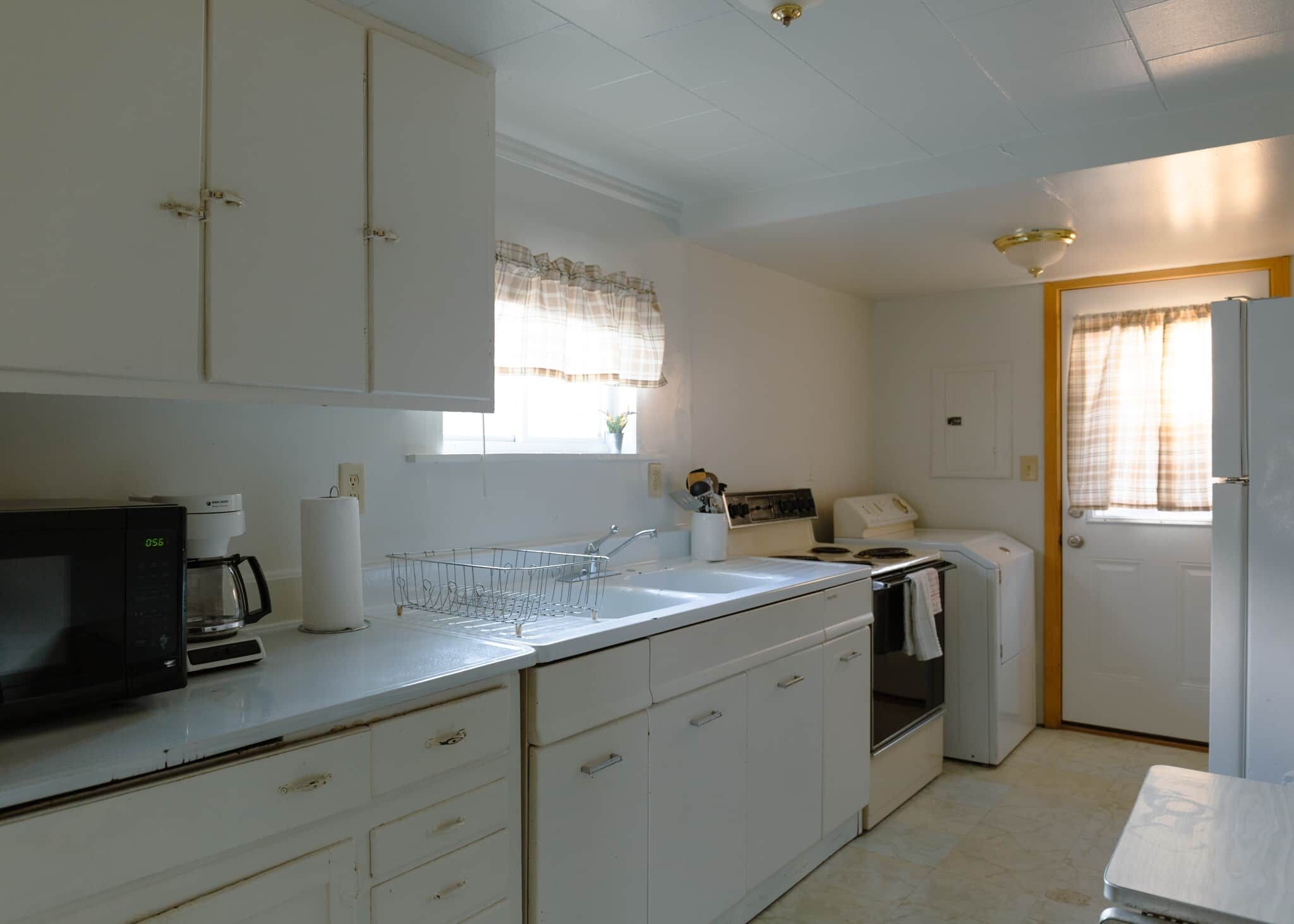 A compact kitchen with white cabinets, a microwave, a sink, and a refrigerator.