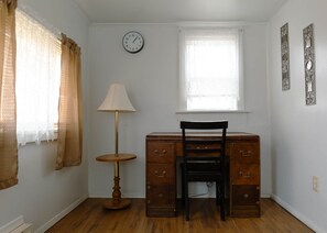 A room with a desk, chair, lamp, window, and clock.