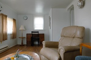 Un salon avec un fauteuil en cuir, un bureau en bois doté de tiroirs, une lampe et une horloge au mur.
