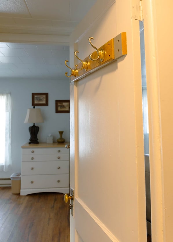 A room with a white door, a wooden dresser, a lamp, and a framed picture on the wall.
